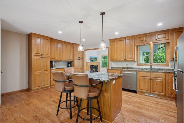 220 Willow Ln, Foley, MN 56329 - kitchen featuring stainless steel appliances, a kitchen island, dark stone counters, a lit fireplace, and light wood finished floors