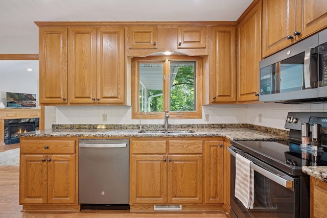 220 Willow Ln, Foley, MN 56329 - kitchen with appliances with stainless steel finishes, light stone countertops, a fireplace, brown cabinetry, and light wood-style floors
