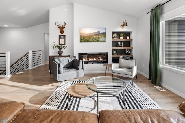 3682 Merrifield Dr S, Fargo, ND 58104 - living room featuring vaulted ceiling, wood finished floors, a glass covered fireplace, baseboards, and built in features