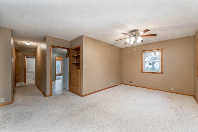 empty room with baseboards, a ceiling fan, a textured ceiling, and light colored carpet