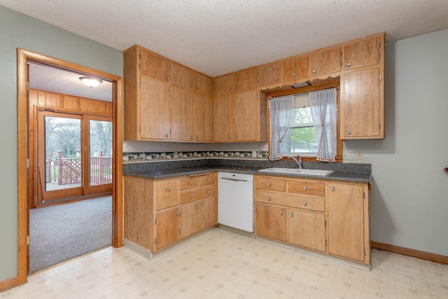 kitchen featuring white dishwasher, dark countertops, a sink, and light floors