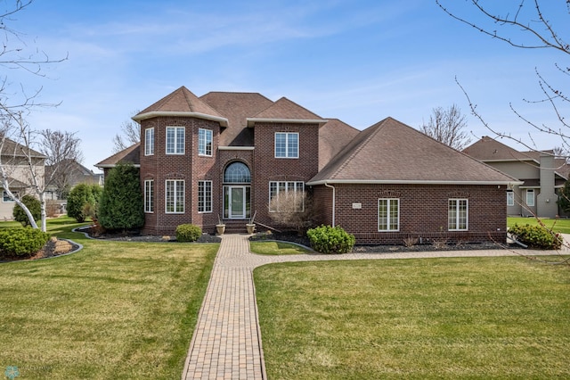 view of front of home with roof with shingles, a front lawn, and brick siding