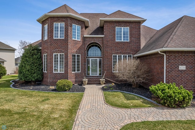 traditional-style home with brick siding, a front lawn, and roof with shingles