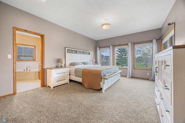 bedroom with light colored carpet, a textured ceiling, baseboards, and ensuite bath