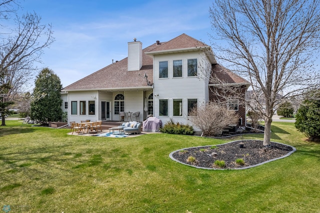 rear view of property featuring a shingled roof, a patio, a chimney, and a lawn