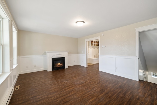 unfurnished living room featuring a wainscoted wall, a baseboard radiator, dark wood-style flooring, and visible vents