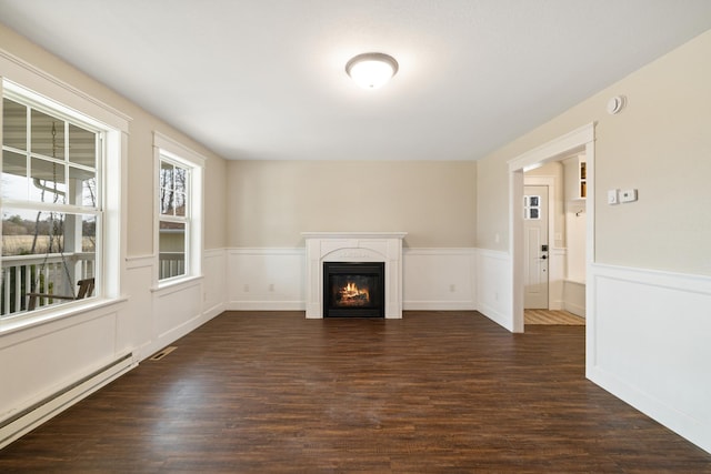 unfurnished living room featuring wainscoting, a baseboard heating unit, a glass covered fireplace, and dark wood-type flooring