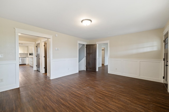 spare room with dark wood finished floors, a decorative wall, and a wainscoted wall