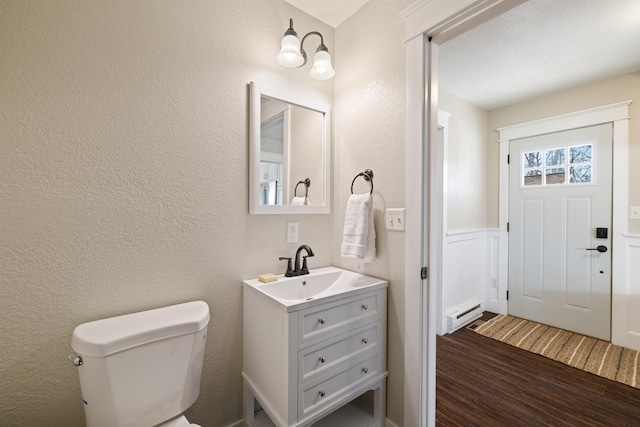 half bath with toilet, a textured wall, wood finished floors, and a baseboard radiator