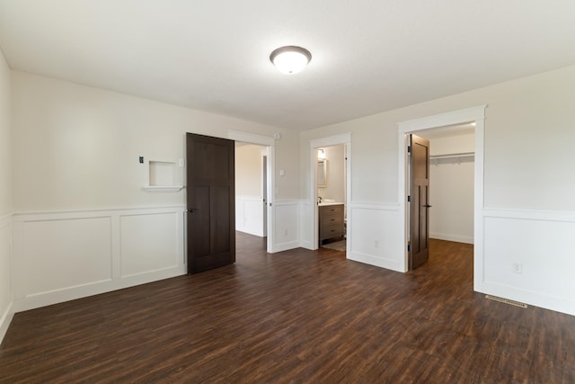 unfurnished bedroom featuring visible vents, a closet, a wainscoted wall, a spacious closet, and dark wood finished floors