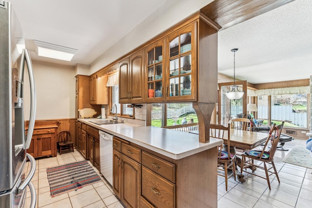 kitchen featuring brown cabinets, dishwasher, light countertops, a sink, and stainless steel fridge