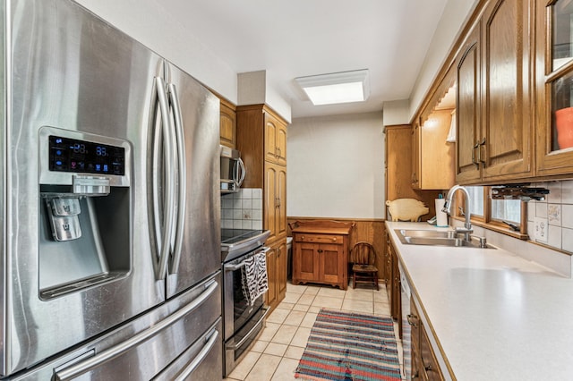 kitchen with backsplash, appliances with stainless steel finishes, a sink, light tile patterned floors, and light countertops