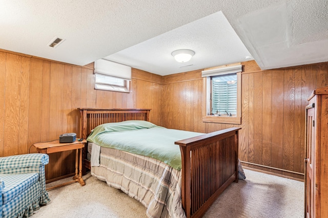 bedroom with light colored carpet, a textured ceiling, visible vents, and wood walls