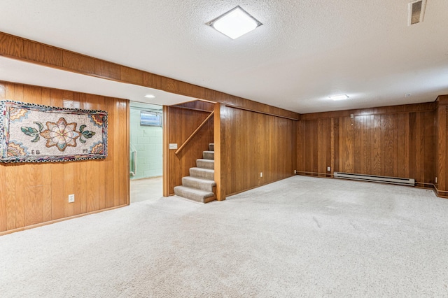 finished below grade area with wood walls, stairs, a textured ceiling, a baseboard heating unit, and carpet
