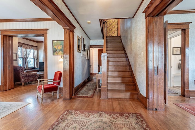 staircase with crown molding, wallpapered walls, and wood finished floors