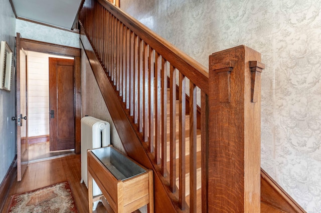 stairs with baseboards, wallpapered walls, radiator heating unit, and wood finished floors