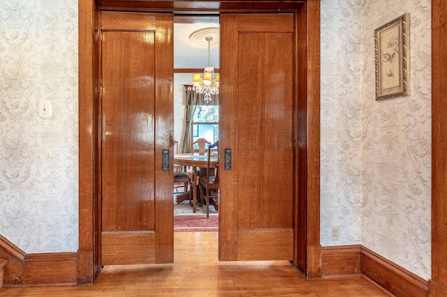 corridor with wallpapered walls, a chandelier, and wood finished floors