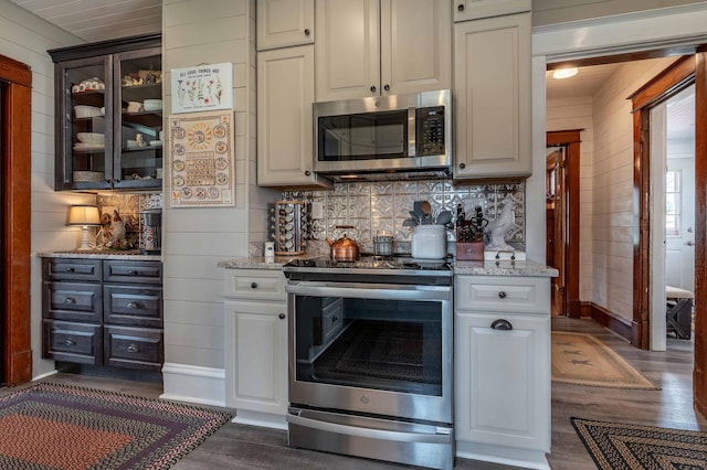 kitchen with wood walls, stainless steel appliances, decorative backsplash, dark wood-style floors, and glass insert cabinets