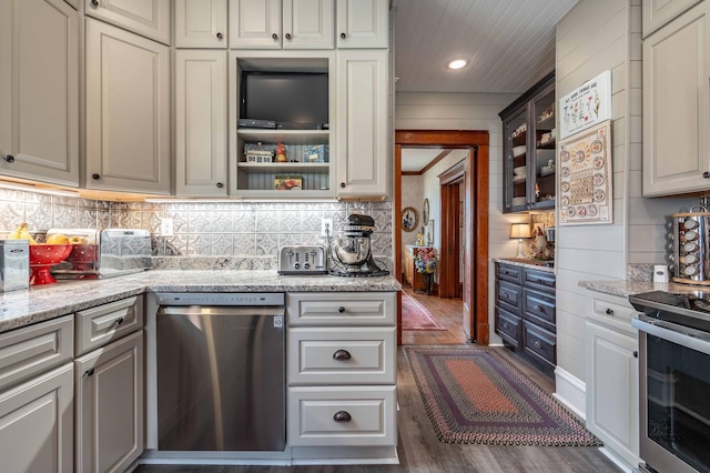 kitchen featuring backsplash, appliances with stainless steel finishes, light stone countertops, dark wood-style floors, and glass insert cabinets