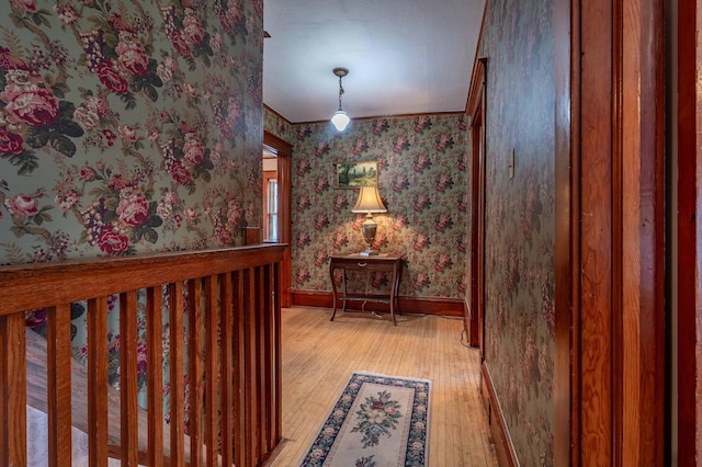 hallway featuring baseboards, light wood finished floors, and wallpapered walls
