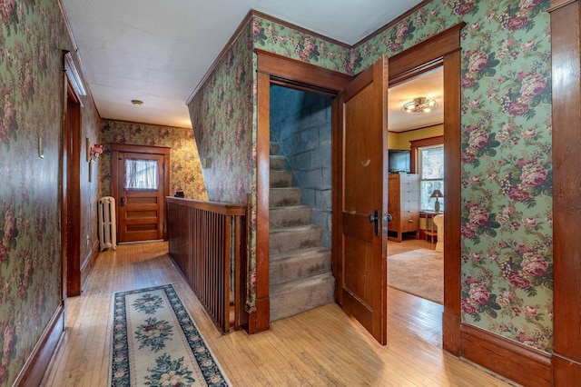 hall with light wood-style floors, stairway, and wallpapered walls