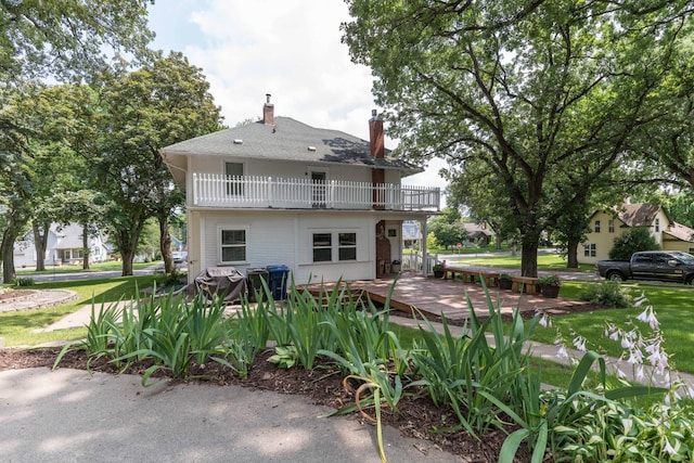 rear view of property with a chimney, a yard, and a balcony