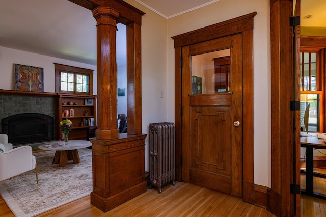 1043 Lincoln Ave, Saint Paul, MN 55105 - entryway featuring radiator heating unit, decorative columns, light wood-style flooring, a fireplace with raised hearth, and ornamental molding