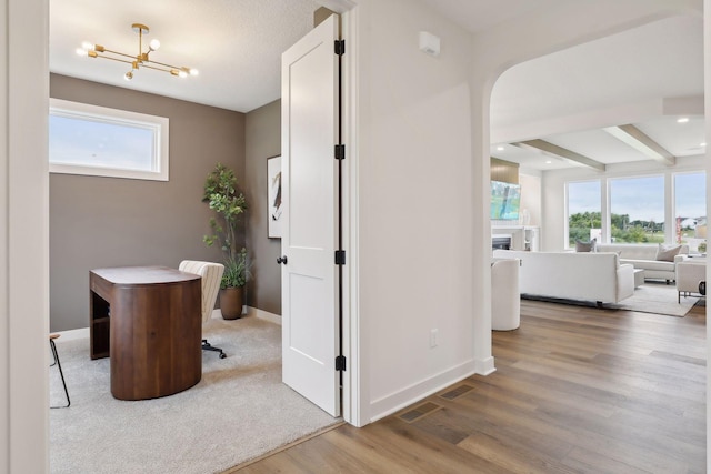 hall featuring baseboards, plenty of natural light, wood finished floors, and a notable chandelier