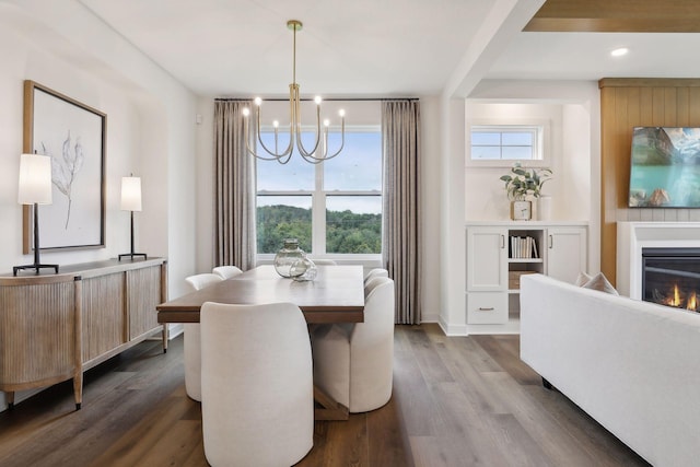 dining space featuring an inviting chandelier, dark wood-type flooring, a glass covered fireplace, and a wealth of natural light