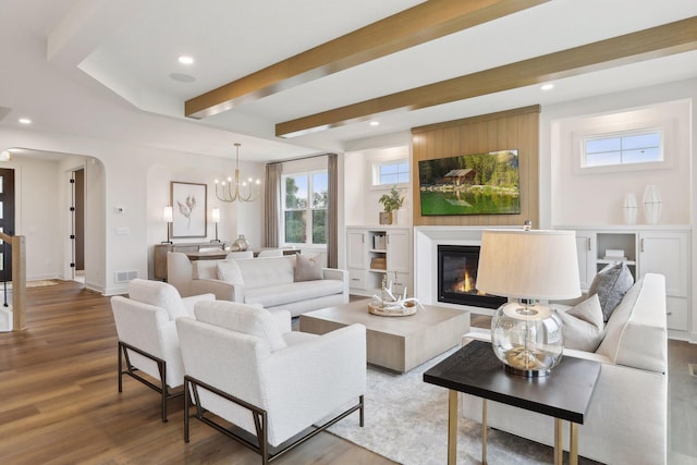 living area featuring visible vents, arched walkways, wood finished floors, a notable chandelier, and a glass covered fireplace