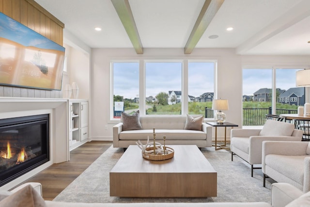 living area featuring a glass covered fireplace, recessed lighting, baseboards, wood finished floors, and beamed ceiling