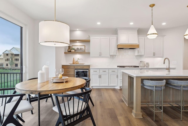 kitchen featuring open shelves, a sink, light countertops, custom exhaust hood, and light wood finished floors