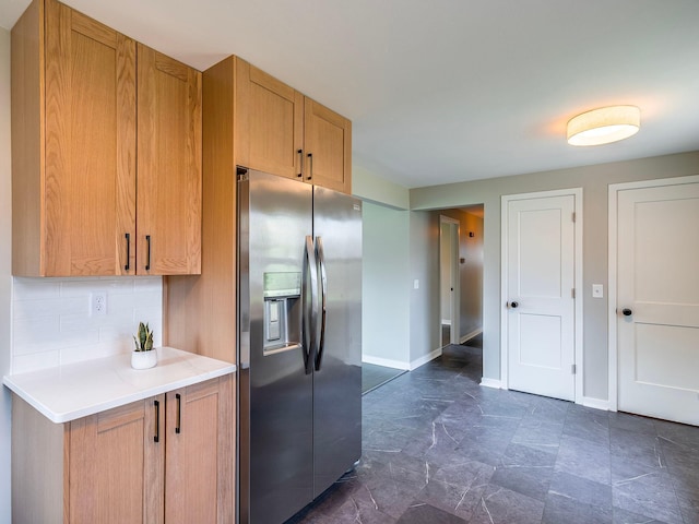 kitchen featuring light countertops, brown cabinetry, baseboards, backsplash, and stainless steel refrigerator with ice dispenser