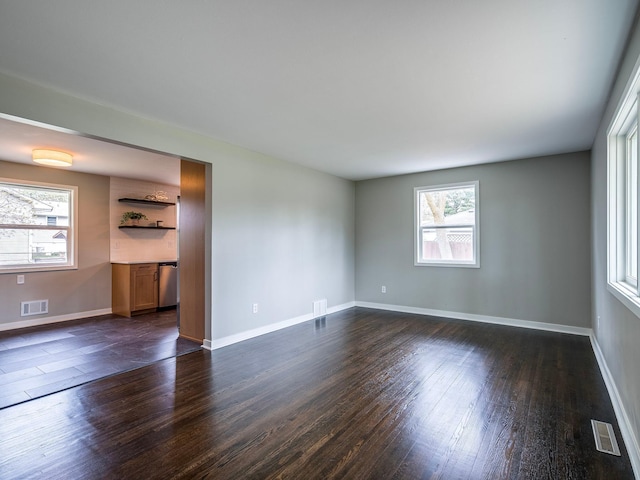 unfurnished room featuring visible vents, a healthy amount of sunlight, and dark wood finished floors