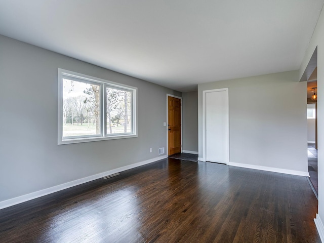 empty room with baseboards, dark wood-style floors, and visible vents