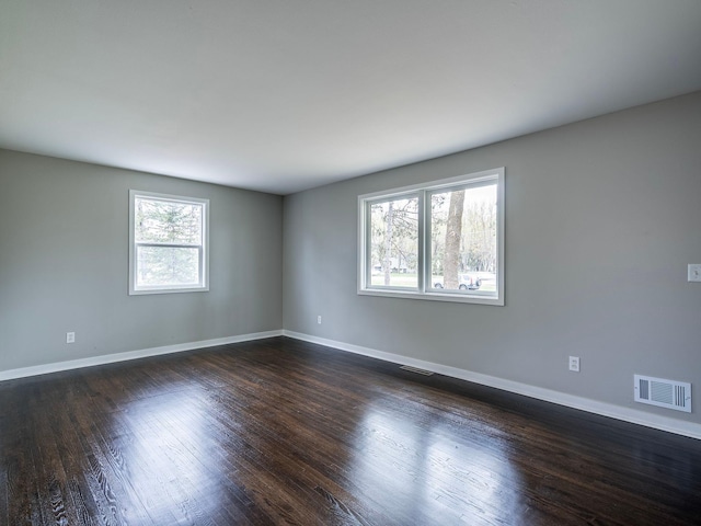 spare room with baseboards, dark wood-style floors, and visible vents