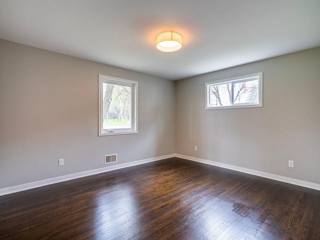 empty room with baseboards, visible vents, plenty of natural light, and dark wood finished floors