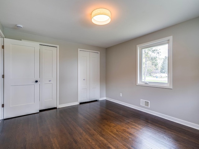 unfurnished bedroom with visible vents, baseboards, two closets, and dark wood-style floors