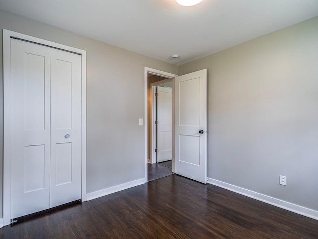 unfurnished bedroom with a closet, baseboards, and dark wood-type flooring