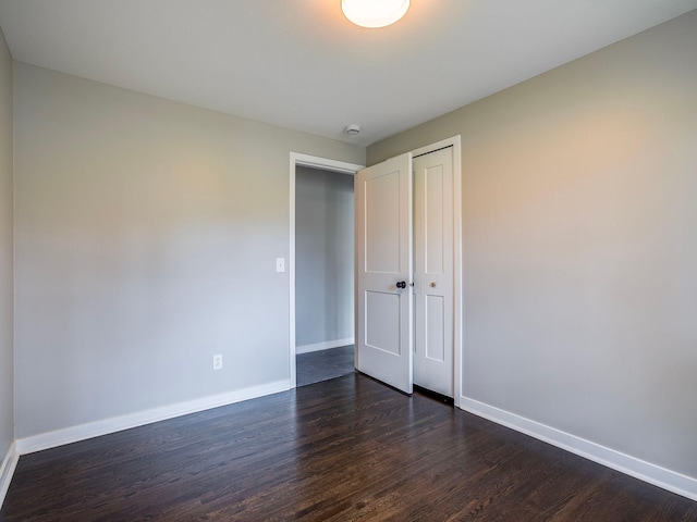 unfurnished bedroom featuring baseboards, a closet, and dark wood-style floors