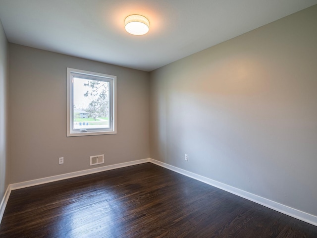 empty room with baseboards, dark wood-type flooring, and visible vents
