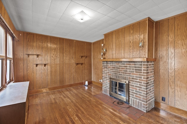 unfurnished living room with baseboards, wood walls, a brick fireplace, and hardwood / wood-style floors