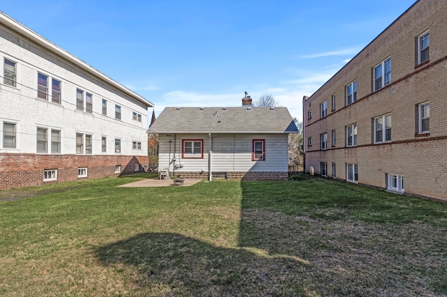 back of property with a lawn, a chimney, a patio area, and roof with shingles