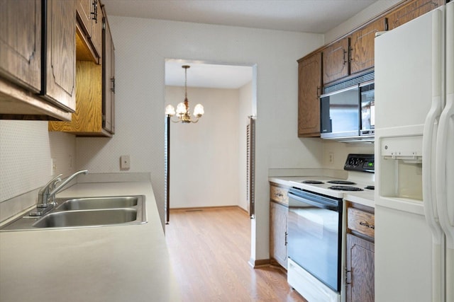 kitchen featuring white appliances, light wood-style floors, light countertops, a sink, and a notable chandelier