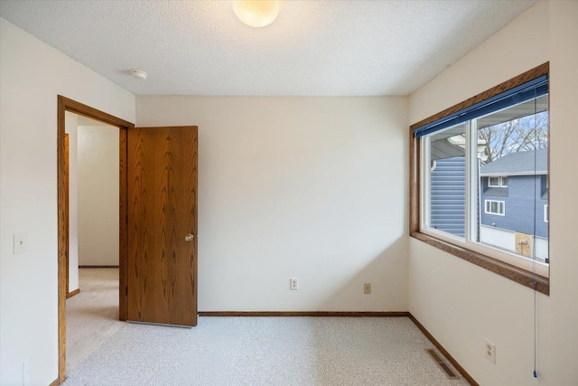 empty room with baseboards, light carpet, a textured ceiling, and visible vents