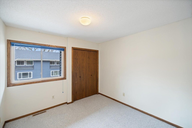 spare room with baseboards, light carpet, a textured ceiling, and visible vents