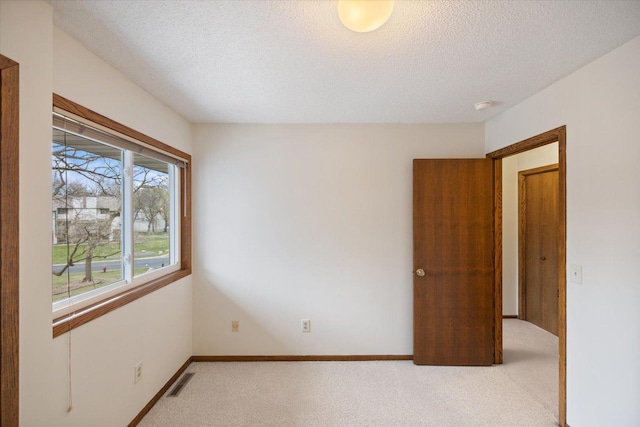 empty room with visible vents, a textured ceiling, baseboards, and light carpet