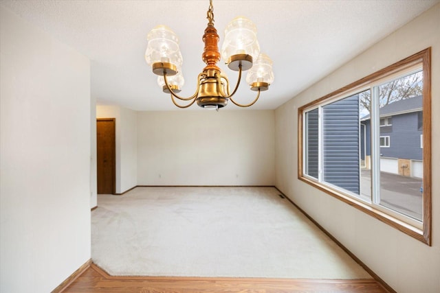 empty room with an inviting chandelier, baseboards, and light carpet