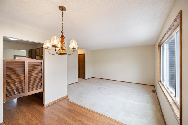 unfurnished dining area featuring baseboards, a textured ceiling, wood finished floors, and a chandelier