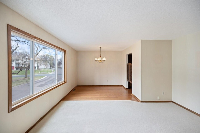 empty room with a textured ceiling, baseboards, an inviting chandelier, and light carpet